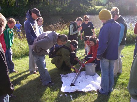 Group of students gathered around a mental rod containing water samples
