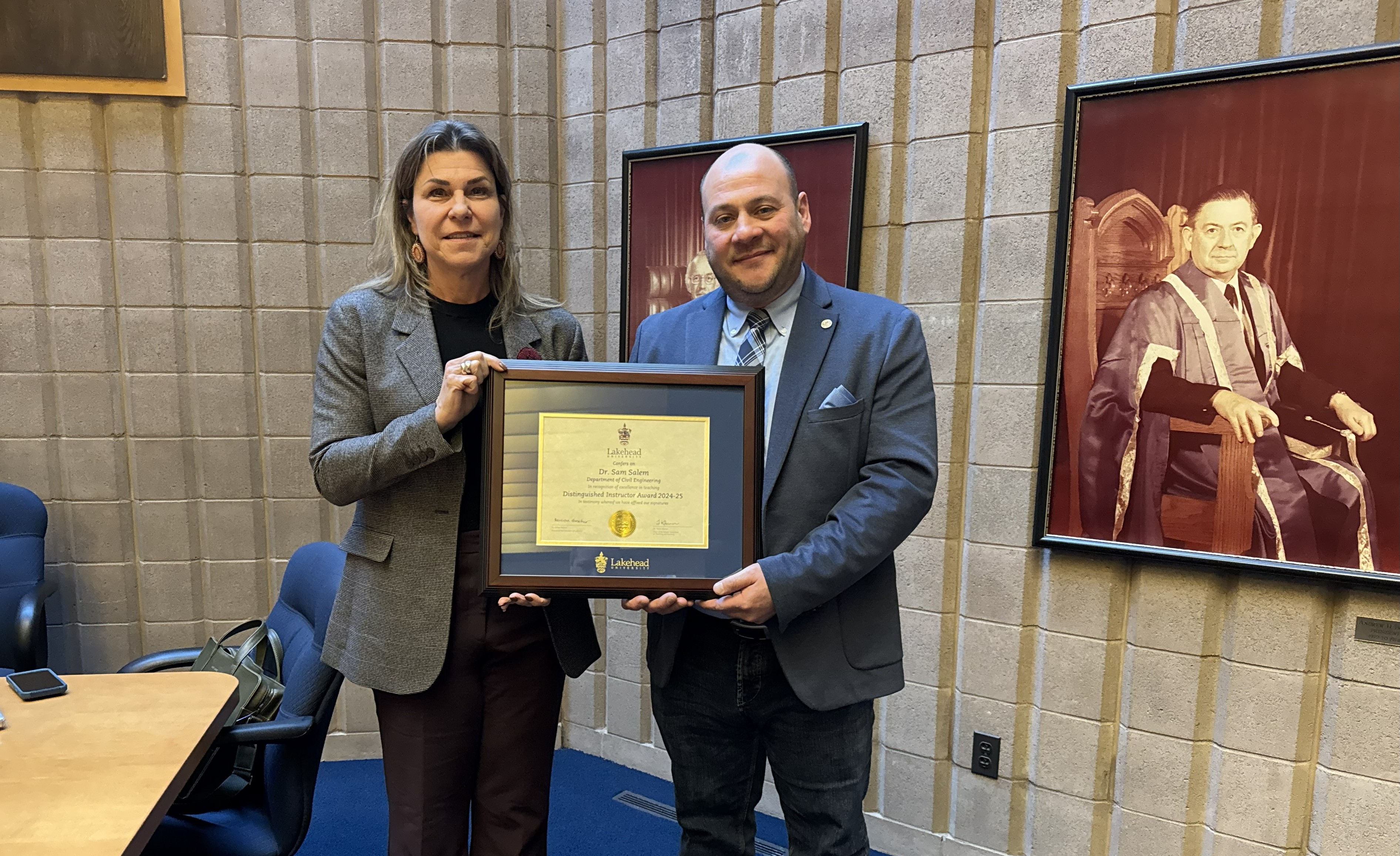 Dr. Sam Salem with Distinguished Instructor Certificate Dr. Gillian Balfour and Dr. Sam Salem stand beside each other in Lakehead University's Senate Chamber holding Dr. Salem's framed 2025 Distinguished Instructor certificate