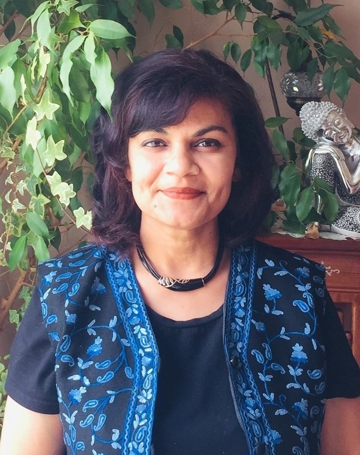 Dr. Roopa Rakshit Dr. Roopa Rakshit sits in a room with a houseplant and a small statue of Buddha in the background