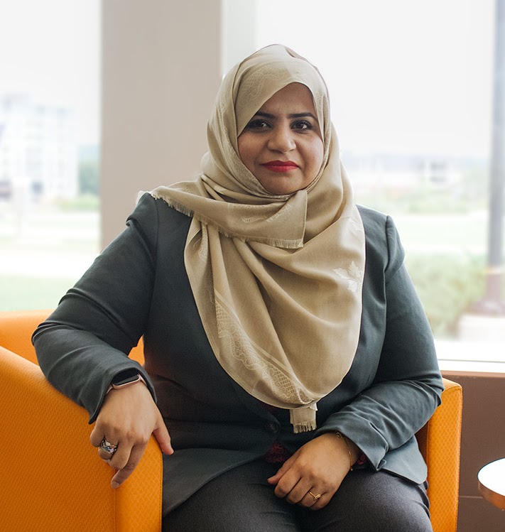 Sana Sharif Seated in Chair Sana Sharif sits in a chair in front of a large window