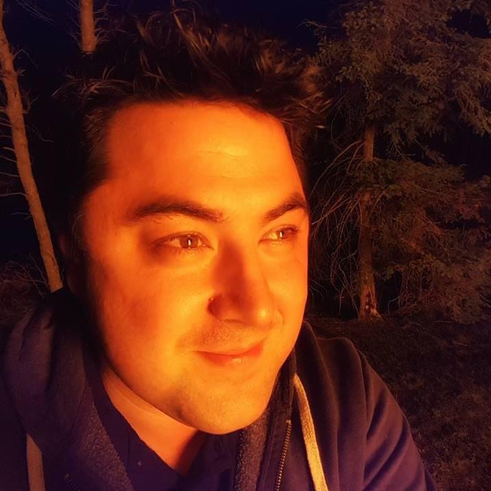 Picture of a man with dark brown hair with an evening forest behind him.